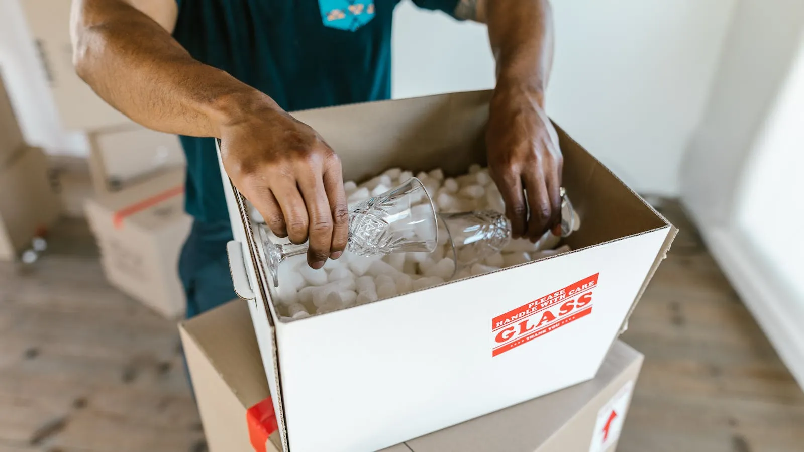 Mover packing crystal glasses in a box with packing peanuts, marked Glass (stock photo)