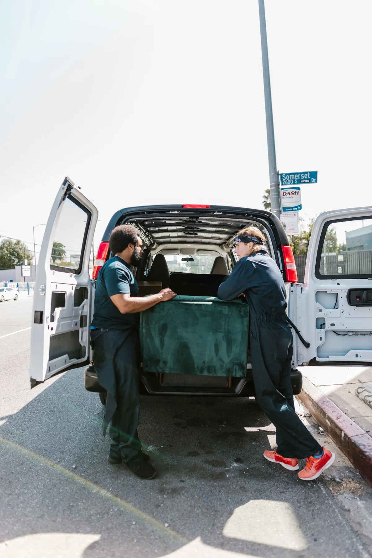 Two movers loading a green sofa into the back of a cargo van